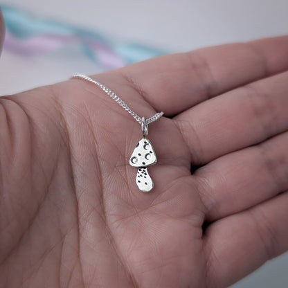 Tiny handmade sterling silver necklace with a mushroom pendant held in a hand against a blurred pastel background